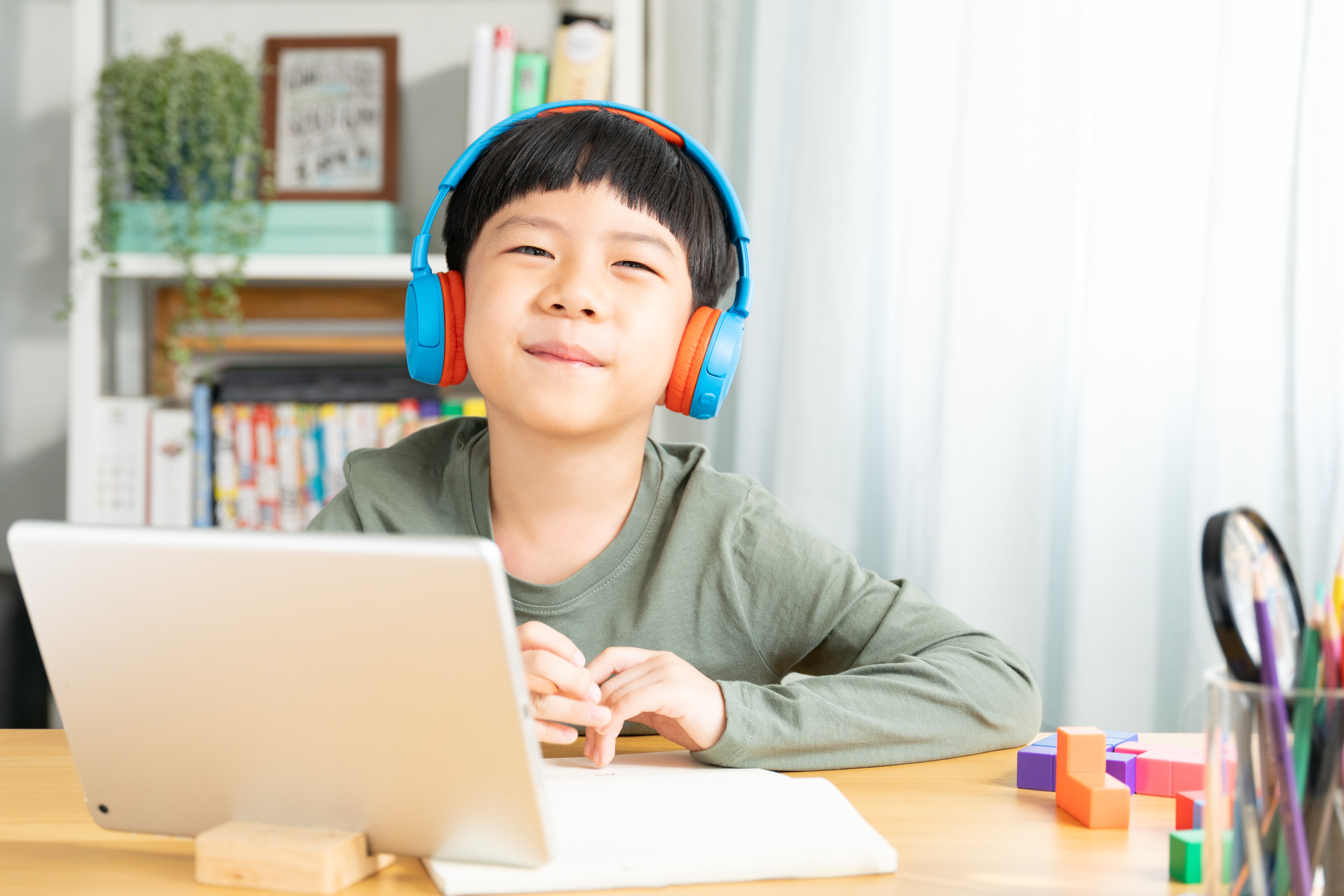 Cute, smart looking Asian boy study online learning with computer tablet, smile and look at camera